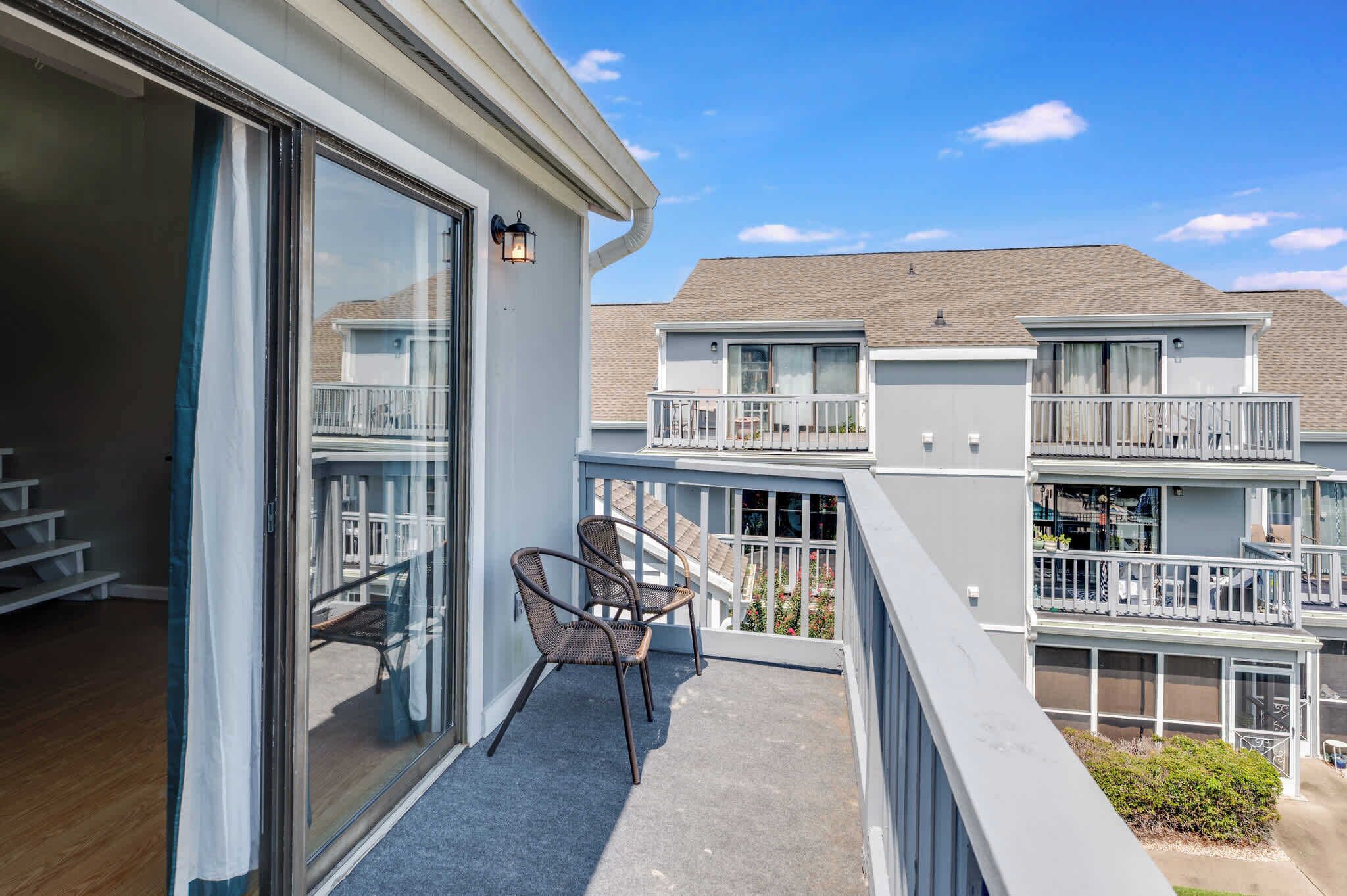 A balcony with two wicker chairs, a glass door, and a view of neighboring buildings.