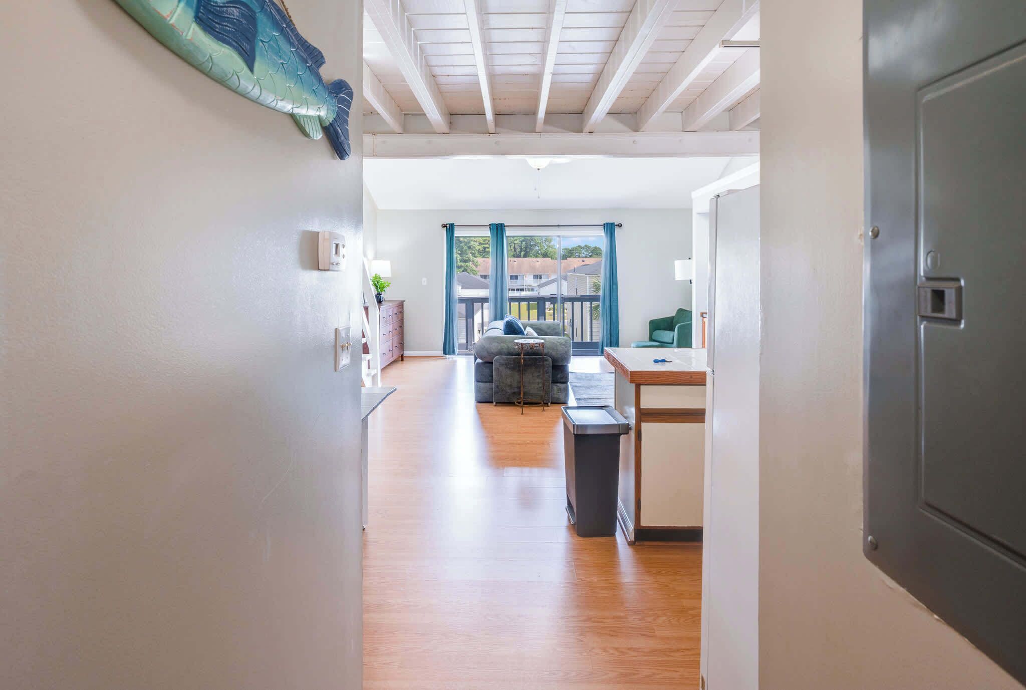 A hallway leading to a living area with a sofa, a small table, and a view through a window.