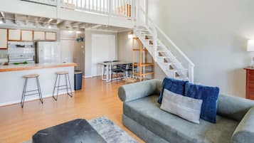 A spacious living area with a kitchen, dining table, and a staircase leading to an upper level.