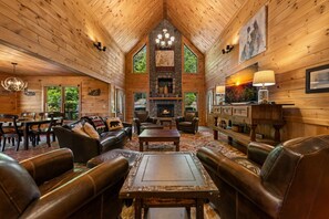 A log cabin interior with a fireplace, leather furniture, and a stone fireplace surround. - Copper Top - Mountain Views | Hot Tub | Expansive Patio (Blue Ridge)
