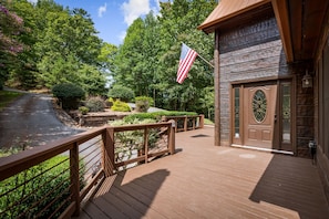A wooden deck with a railing, a flag, and a building with a door. - Copper Top - Mountain Views | Hot Tub | Expansive Patio (Blue Ridge)