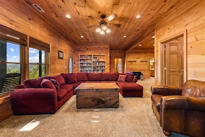 A log cabin interior with a sectional sofa, a coffee table, leather chairs, a ceiling fan, and a bookshelf. - Copper Top - Mountain Views | Hot Tub | Expansive Patio (Blue Ridge)