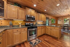 A wooden cabin-style kitchen with granite countertops, stainless steel appliances, and a dining area with a view. - Copper Top - Mountain Views | Hot Tub | Expansive Patio (Blue Ridge)