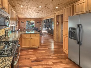 A kitchen with wooden cabinets, a granite countertop, a stainless steel refrigerator, and a stone fireplace. - Copper Top - Mountain Views | Hot Tub | Expansive Patio (Blue Ridge)