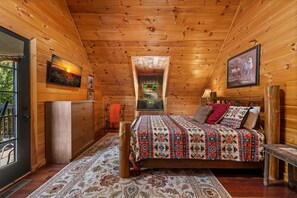 A cozy log cabin bedroom with a bed, a window, a dresser, and a painting on the wall. - Copper Top - Mountain Views | Hot Tub | Expansive Patio (Blue Ridge)