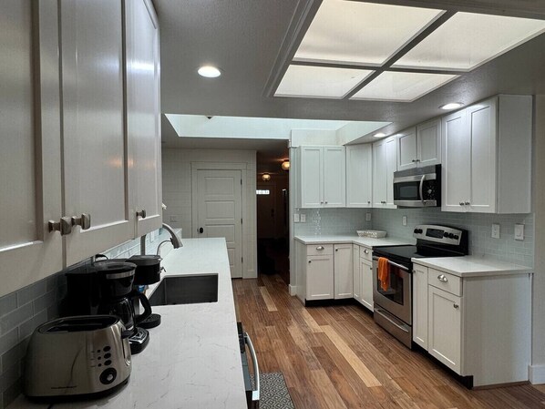 A modern kitchen with white cabinets, a microwave, an oven, and a coffee maker.