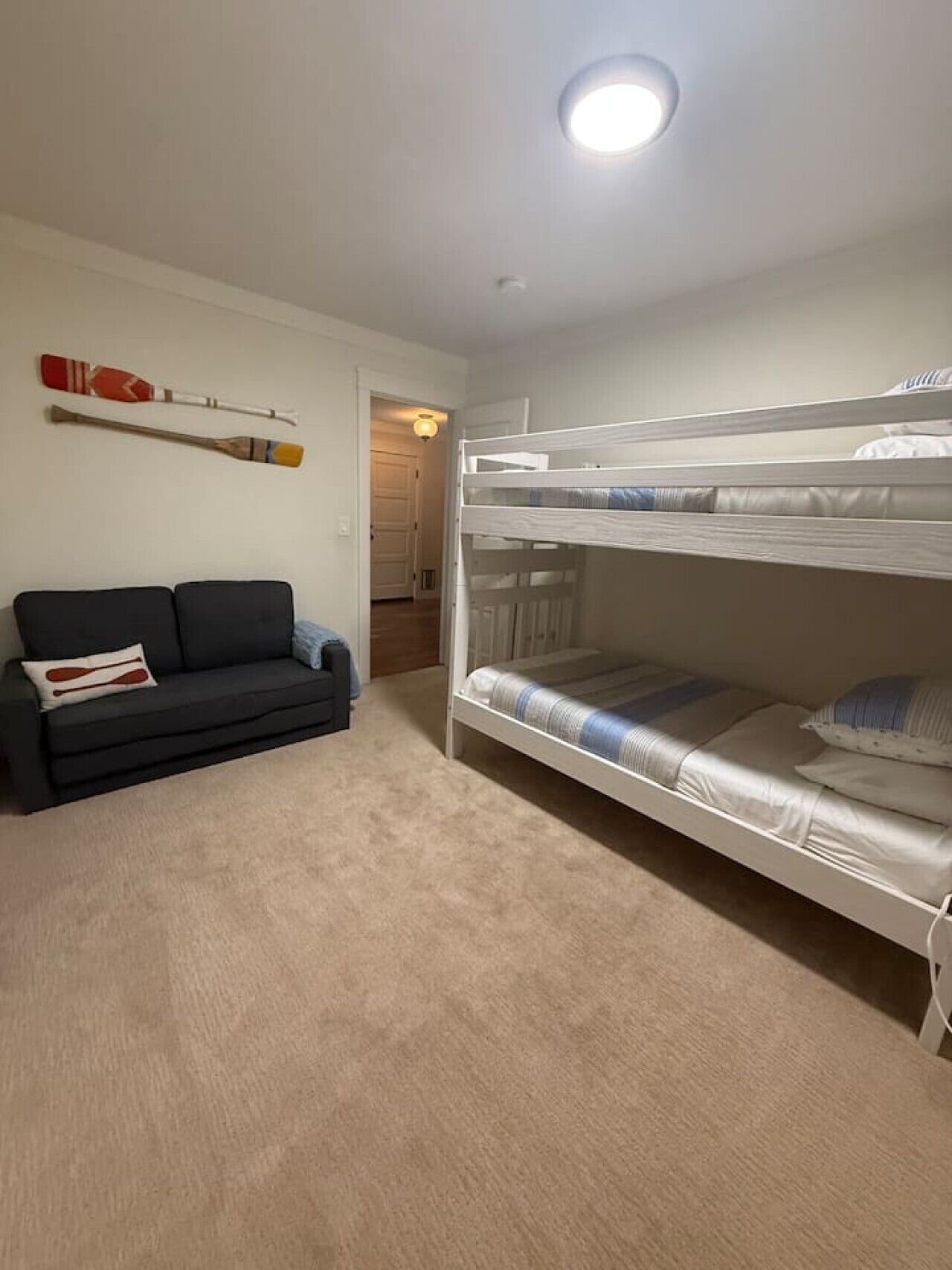 A room with a bunk bed, a sofa, and a wall-mounted paddleboard.