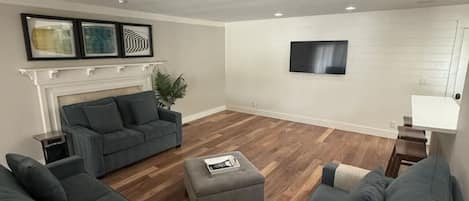 A modern living room with a fireplace, a flat-screen TV mounted on the wall, and a large window.