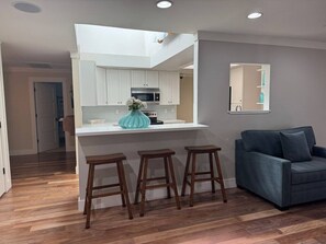 A modern kitchen with white cabinets, a central island with stools, and a dark blue sofa in a living area.