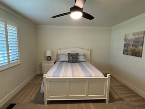 A bedroom with a bed, a nightstand, a lamp, a ceiling fan, and a window with blinds.