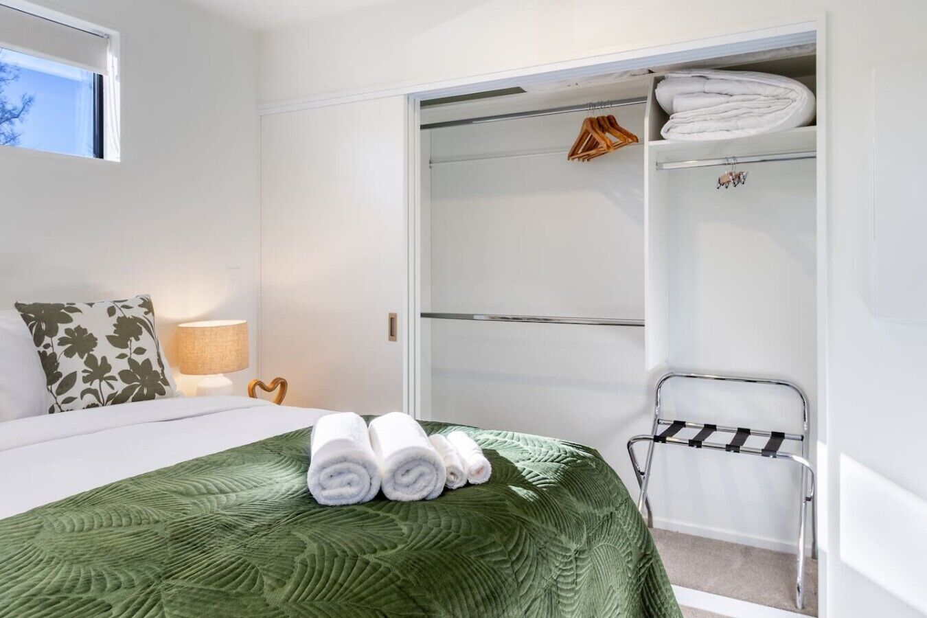 A hotel room with a bed, a green bedspread, a set of towels, a wardrobe, and a chair.