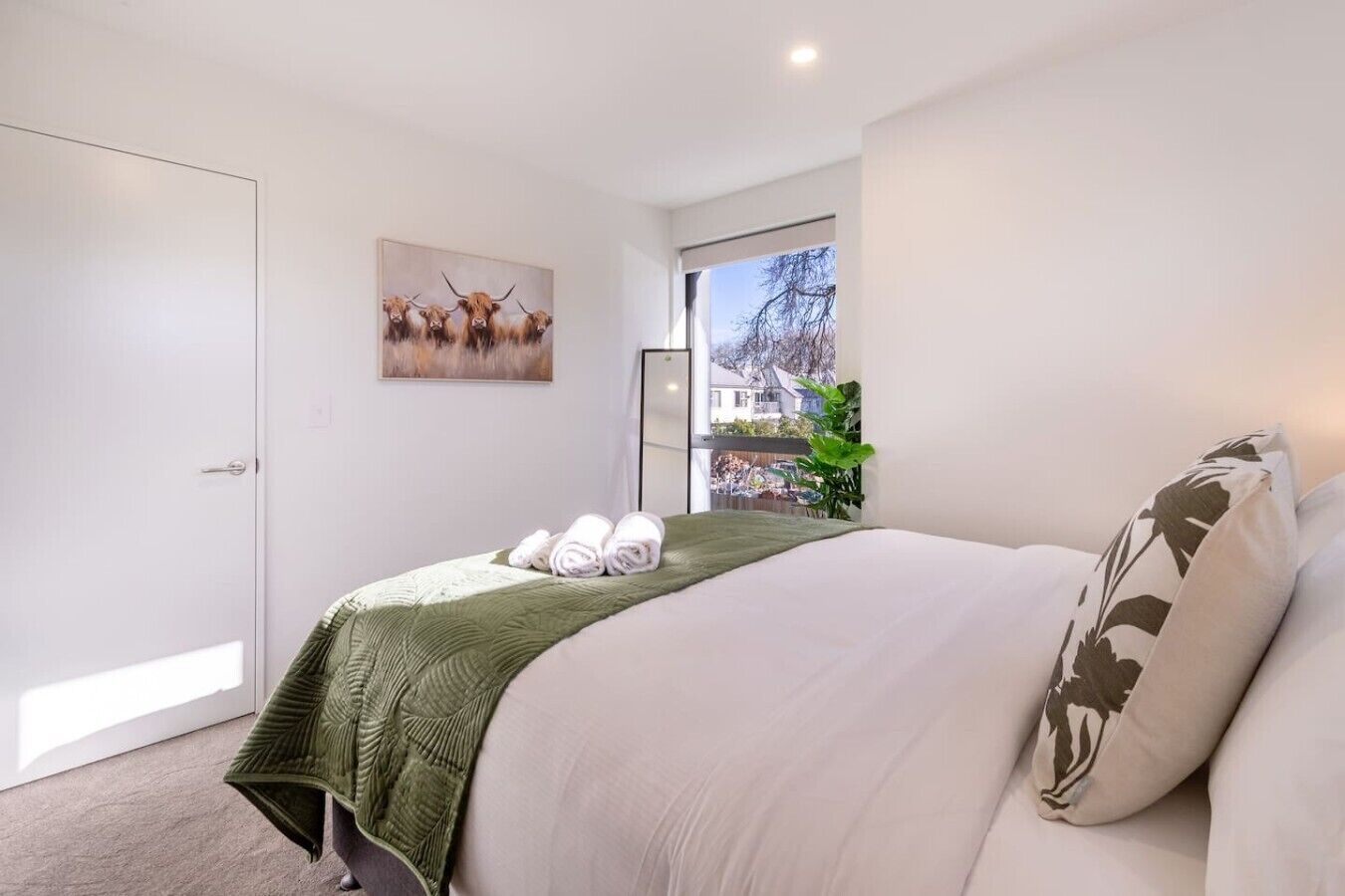 A bedroom with a bed, a door, a window, and a painting on the wall.