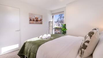 A bedroom with a bed, a door, a window, and a painting on the wall.