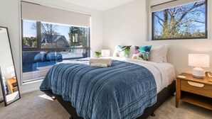 A bedroom with a large bed, a bedside table, a nightstand, and a window with a view of a residential area. - Peaceful Family CBD Stay w/ Car Park + EV charger (Christchurch)