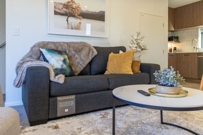 Ein Wohnzimmer mit Schlafsofa, rundem Couchtisch, Fernbedienung und Blumentopf.