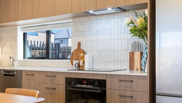 A modern kitchen with wooden cabinets, a built-in oven, and a stainless steel refrigerator. - Peaceful Family CBD Stay w/ Car Park + EV charger (Christchurch)