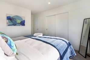 A bedroom with a bed, a bedside table, a mirror, and a door. - Peaceful Family CBD Stay w/ Car Park + EV charger (Christchurch)