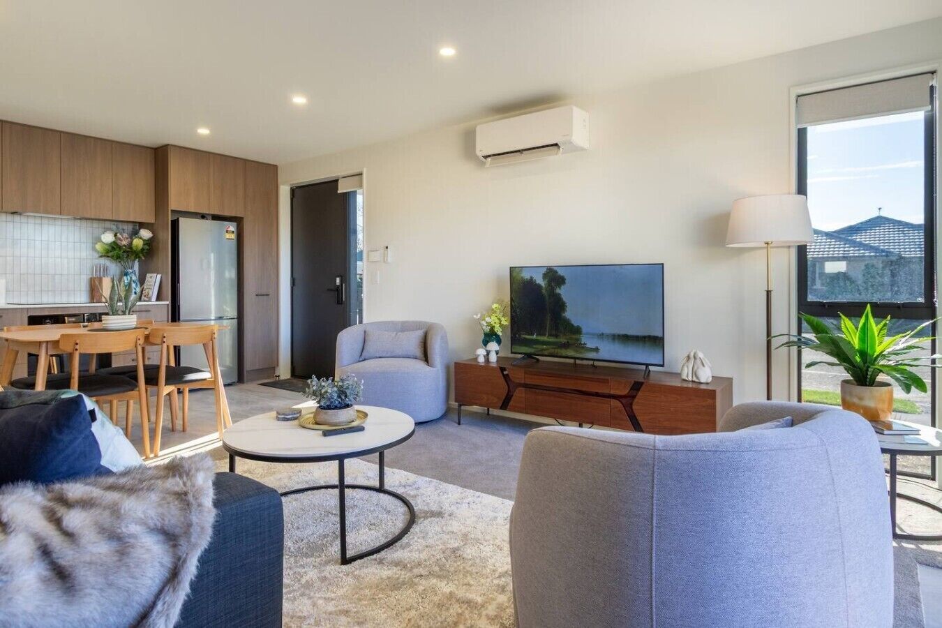 A modern living room with a flat-screen TV, a sofa, a coffee table, and a dining area with chairs.