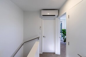 A hallway with a white door, a handrail, and an air conditioning unit mounted on the wall. - Peaceful Family CBD Stay w/ Car Park + EV charger (Christchurch)