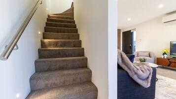 A staircase with carpeted steps and a metal handrail, leading to a living area with a sofa, a coffee table, and a television.