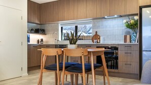 A modern kitchen with wooden cabinets, a dining table with chairs, and a window with a view of the outside. - Peaceful Family CBD Stay w/ Car Park + EV charger (Christchurch)