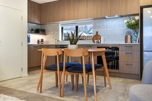 A modern kitchen with wooden cabinets, a dining table with chairs, and a window with a view of the outside. - Peaceful Family CBD Stay w/ Car Park + EV charger (Christchurch)