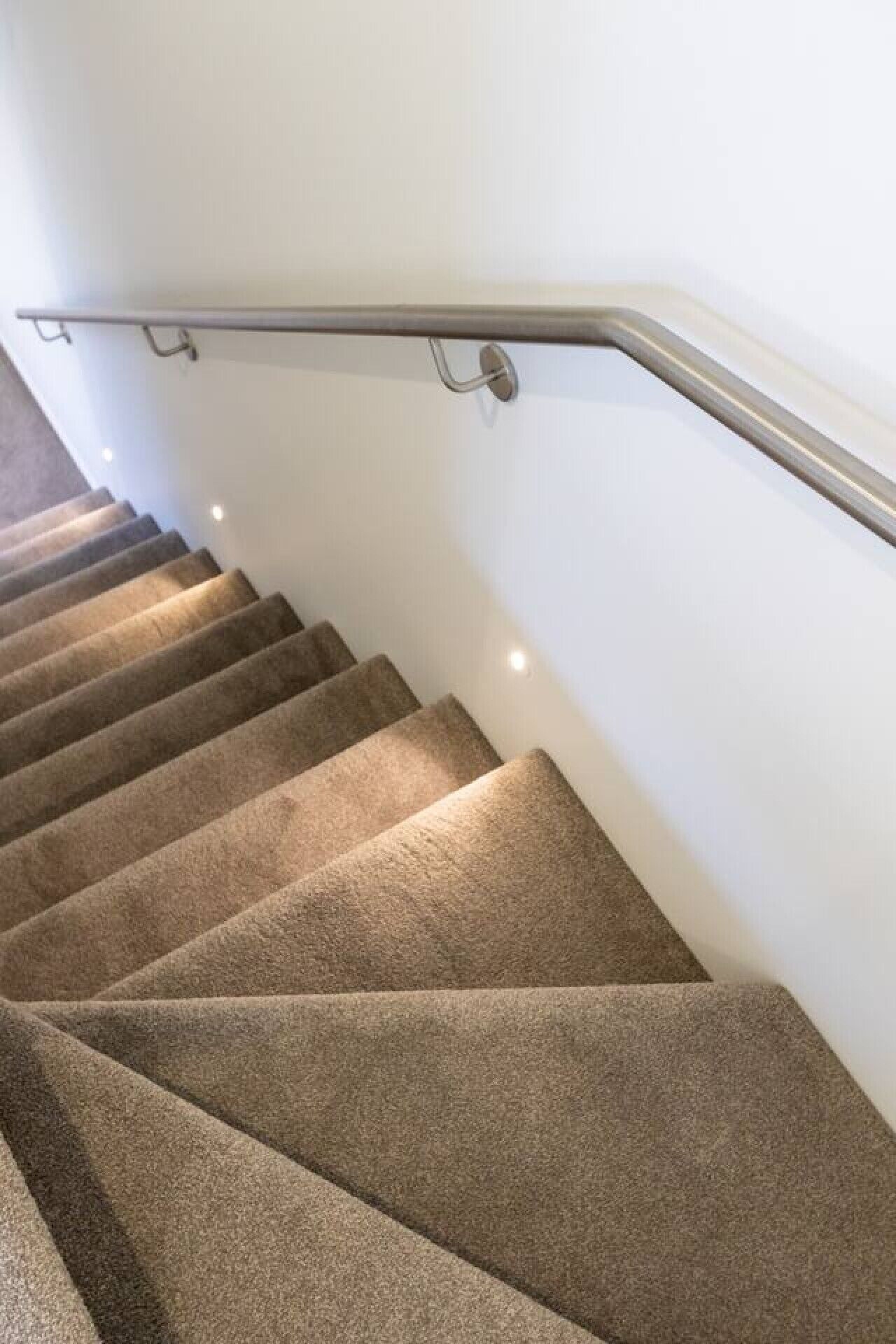 A carpeted staircase with a metal handrail and wall-mounted lighting.