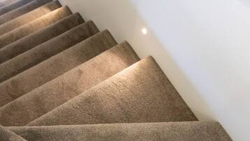 A carpeted staircase with a metal handrail and wall-mounted lighting.