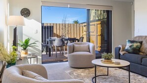 A modern living room with a sofa, armchair, coffee table, and a dining area with chairs and a table. - Peaceful Family CBD Stay w/ Car Park + EV charger (Christchurch)