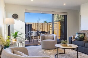 A modern living room with a sofa, armchair, coffee table, and a dining area with chairs and a table. - Peaceful Family CBD Stay w/ Car Park + EV charger (Christchurch)