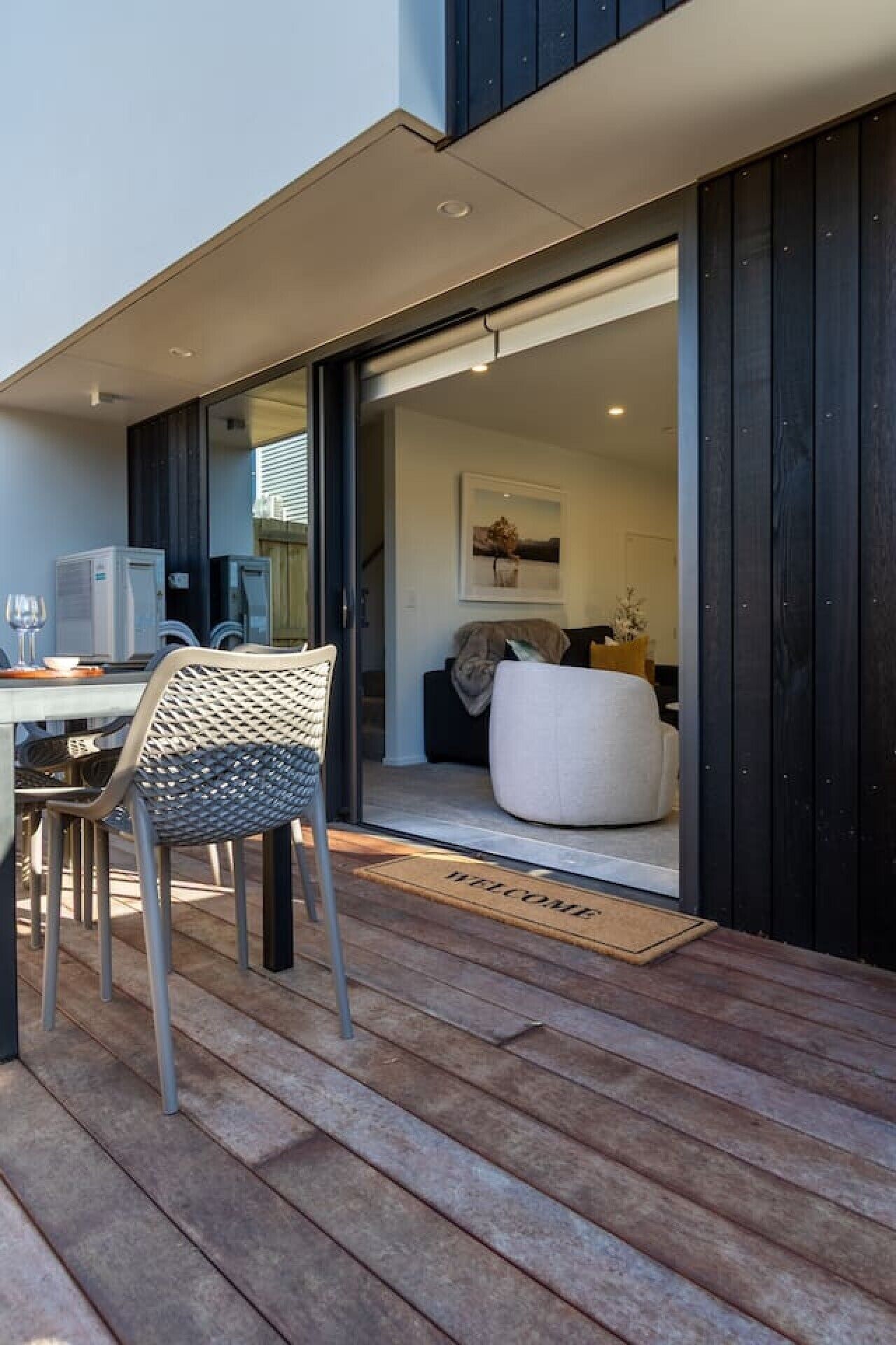 An outdoor patio with a table and chairs, a sliding glass door leading to an interior space with a sofa and a cat.