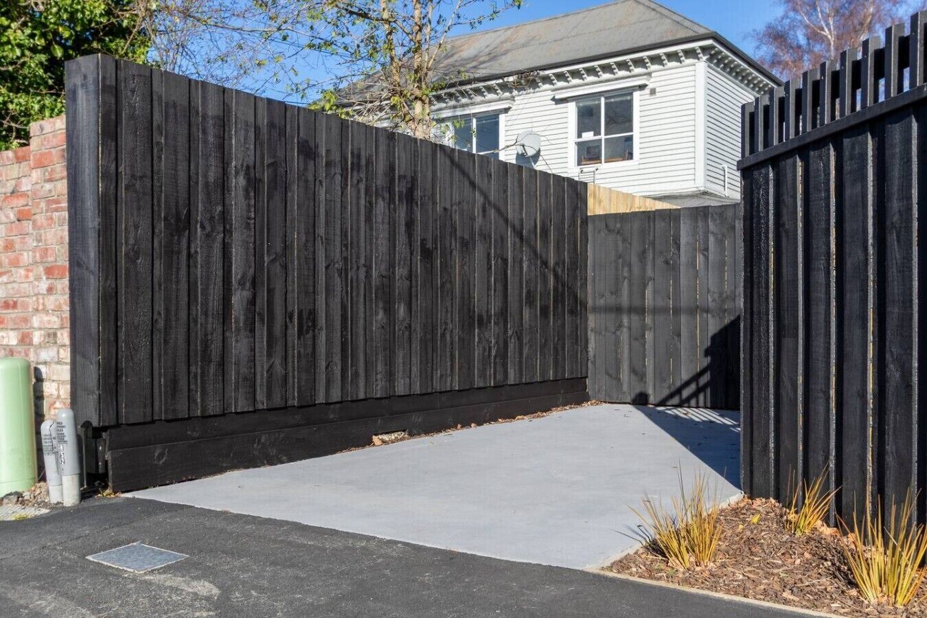 A black metal fence with a concrete driveway leading to a house.