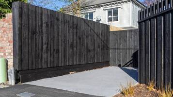 A black metal fence with a concrete driveway leading to a house.