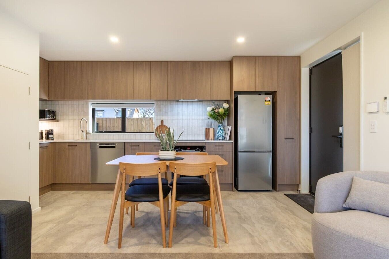 A modern kitchen with wooden cabinets, a stainless steel refrigerator, and a dining area with a table and chairs.