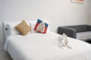 Et hotelværelse med seng, puder, en grå sofa og et håndklæde på sengen.