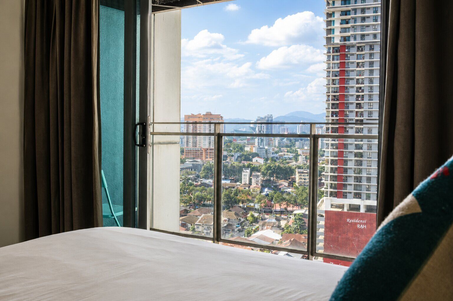 Habitación de hotel con una cama, vista de un paisaje urbano a través de un ventanal y cortinas.