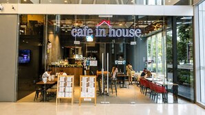 Una cafetería con una decoración moderna, que incluye paredes de vidrio, mesas de madera y un atril para el menú en el exterior.