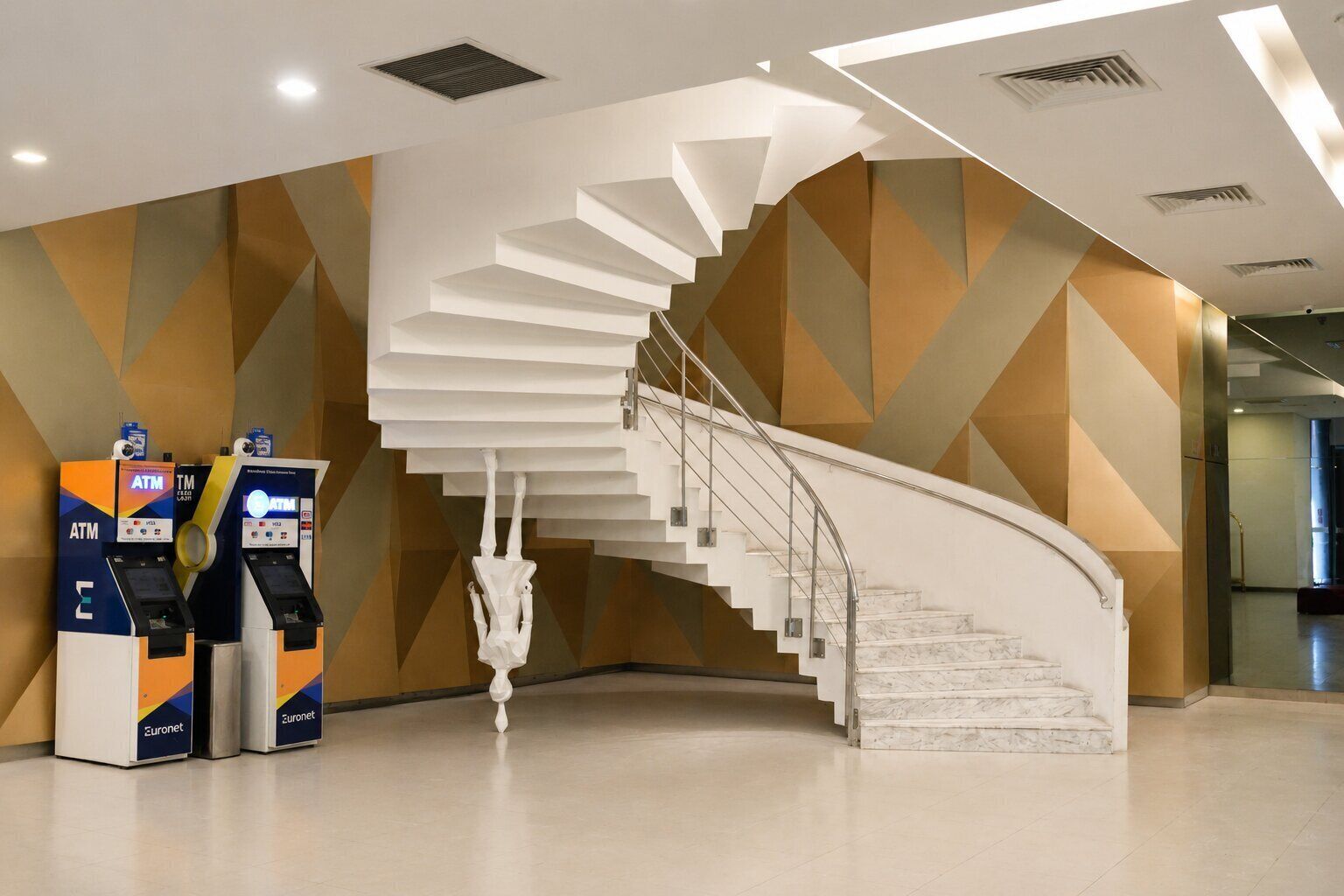 A modern interior with a spiral staircase, ATM machines, and geometric wall patterns.