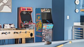 Een pooltafel met een tafelvoetbaltafel en twee speelautomaten voor een blauwe muur.