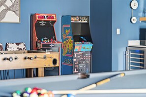 Ein Billardtisch, ein Kicker und zwei Spielautomaten vor einer blauen Wand.