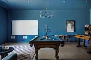 A pool table in a room with blue walls, a projector screen, and a foosball table. - On SoCo:Skyline, Sleeps 16, Game Room, Theater (Austin)
