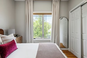 A bedroom with a large window, a bed with pillows, a bedside table with a lamp, and a wardrobe. - On SoCo:Skyline, Sleeps 16, Game Room, Theater (Austin)