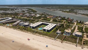 Vista aérea de un complejo turístico costero con un extenso edificio, una playa de arena y un río al fondo.