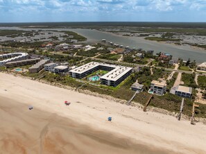 An aerial view of a coastal resort with a large building complex, a sandy beach, and a river in the background. - Thoughtfully Redesigned Beachside Condo (St. Augustine)
