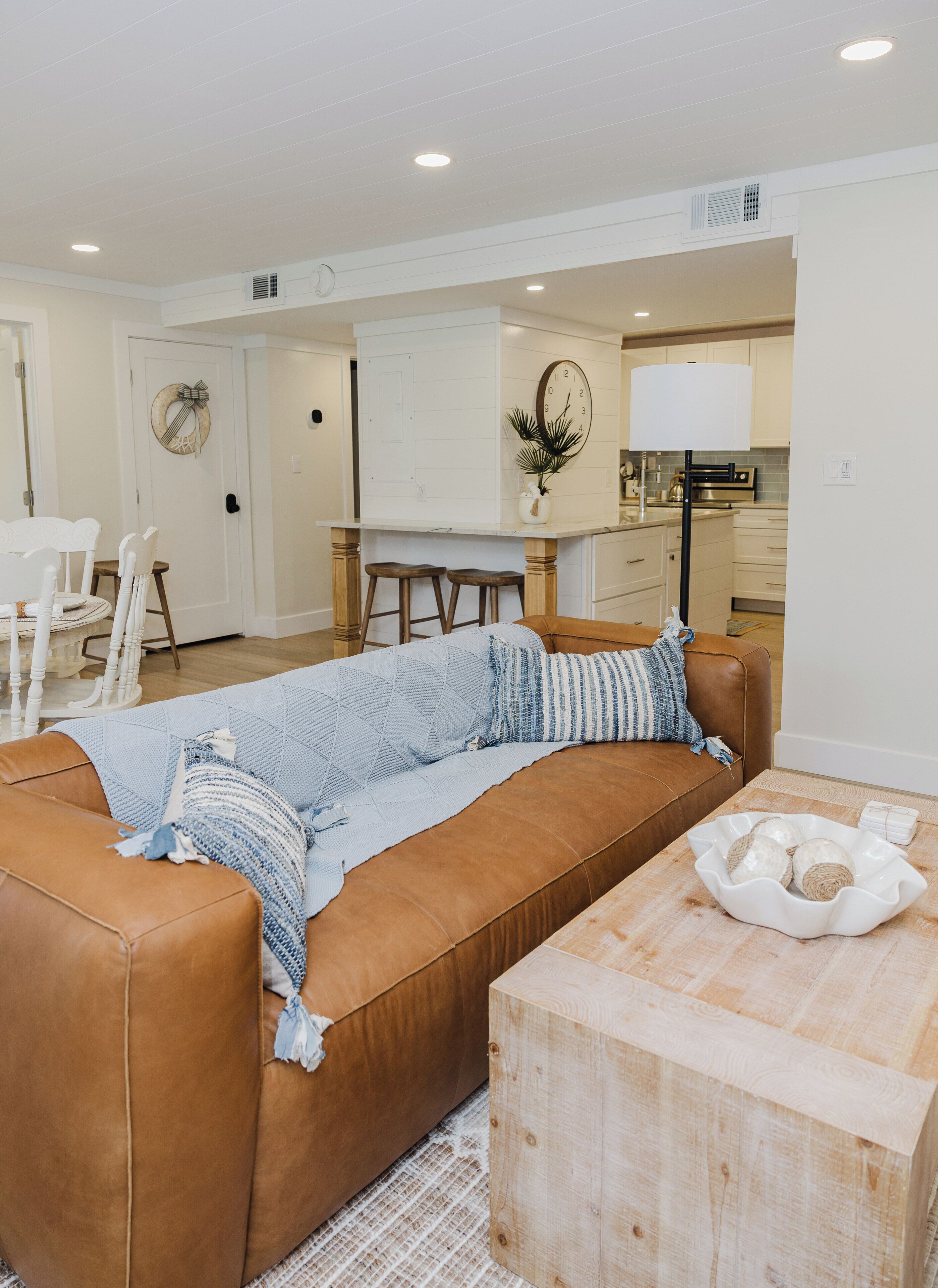 A living room with a brown sofa, a wooden coffee table, and a kitchen area in the background.