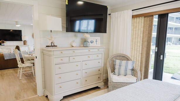 Un dormitorio con cama, cómoda, silla y televisor sobre la cómoda.