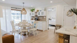 Una cocina moderna con armarios blancos, un comedor con sillas blancas y vistas al exterior.