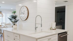 Una cocina moderna con armarios blancos, una isla central, horno empotrado y un reloj en la pared.