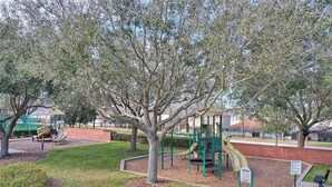 A playground with slides and climbing structures, surrounded by trees and a brick wall. - 6BR Private Pool Home at West Haven Gated Community (Davenport)
