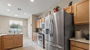 A modern kitchen with wooden cabinets, stainless steel appliances, and a window with blinds. - 6BR Private Pool Home at West Haven Gated Community (Davenport)